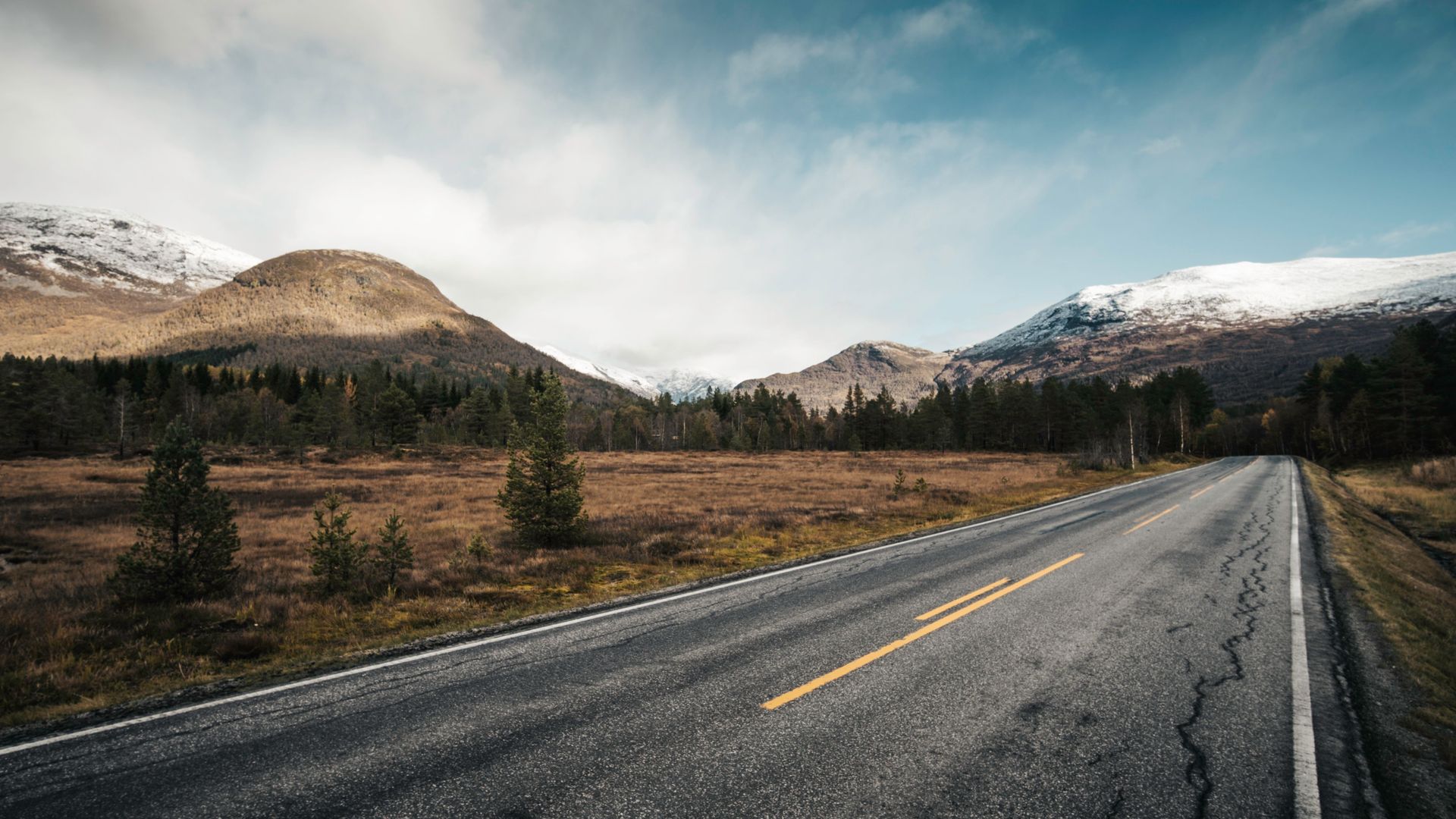 Picturesque mountain road with snow-capped peaks and a clear sky, perfect for travel and adventure themes.