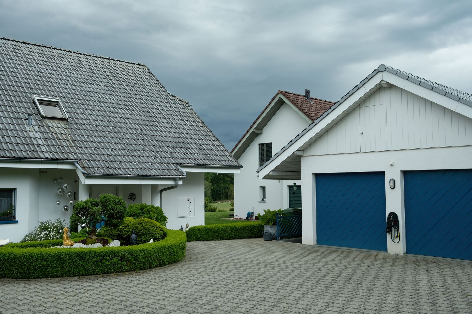 Lovely suburban houses with blue garage doors under cloudy sky, surrounded by greenery.